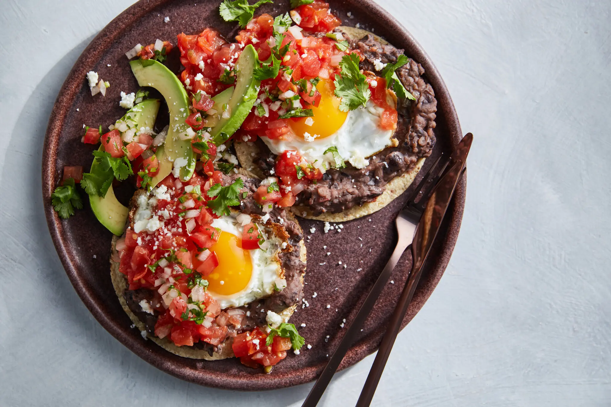 Best Huevos Rancheros (Restaurant-Style) Fried Huevos Rancheros with fresh tomato salsa, avocado slices, and cilantro on a plate.