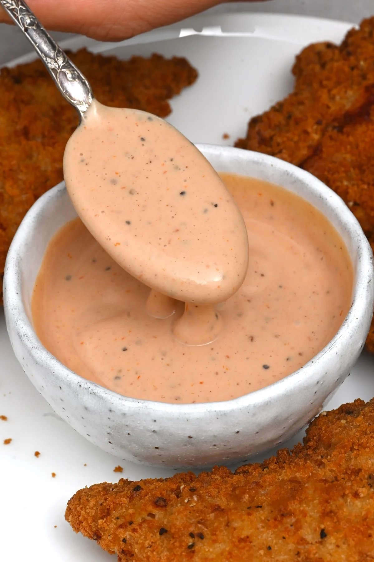Cane’s Sauce Recipe – Best Restaurant-Style Dip A silver spoon dipping into a ceramic bowl filled with creamy burger or cocktail sauce.