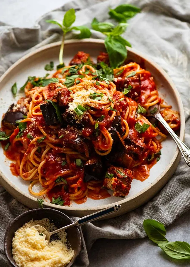 A large plate of spaghetti pasta tossed in a rich red tomato sauce with fresh basil.