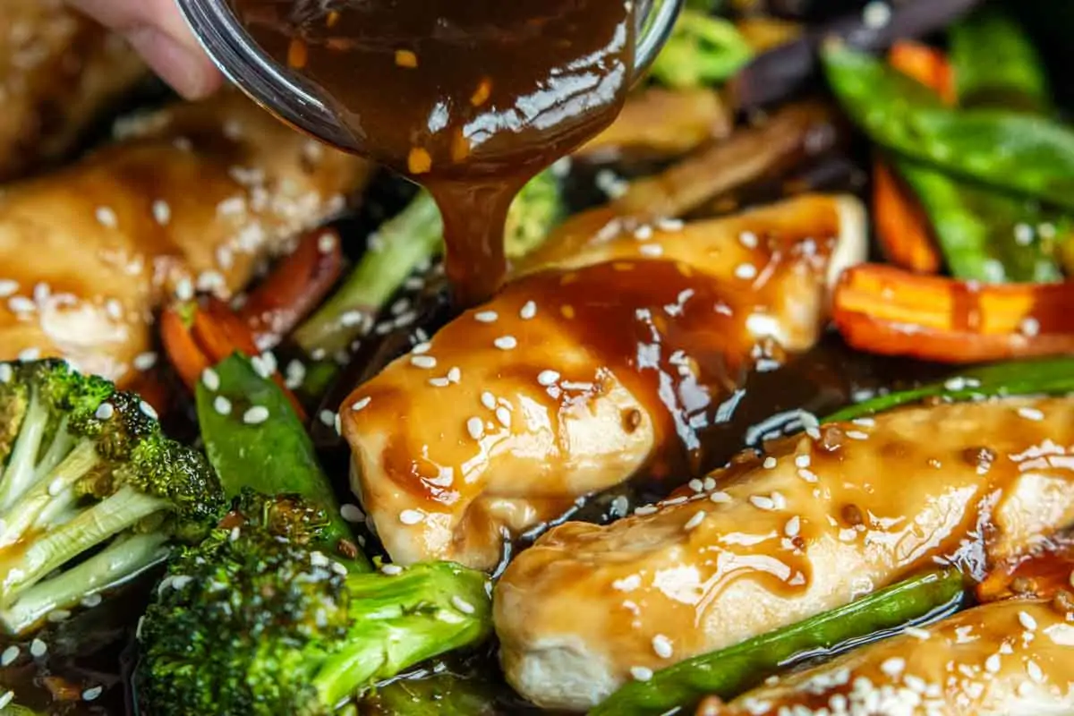Pouring a rich teriyaki or savory glaze over cooked chicken breasts and broccoli.