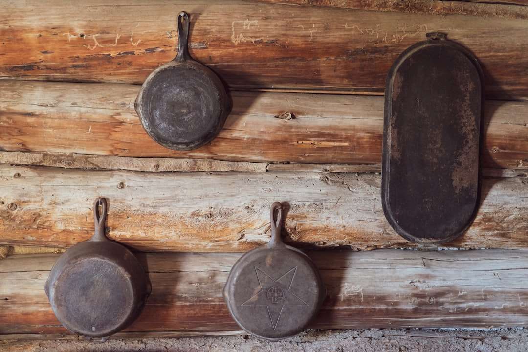 Various sizes of black cast iron skillets hanging on a rustic wooden wall.