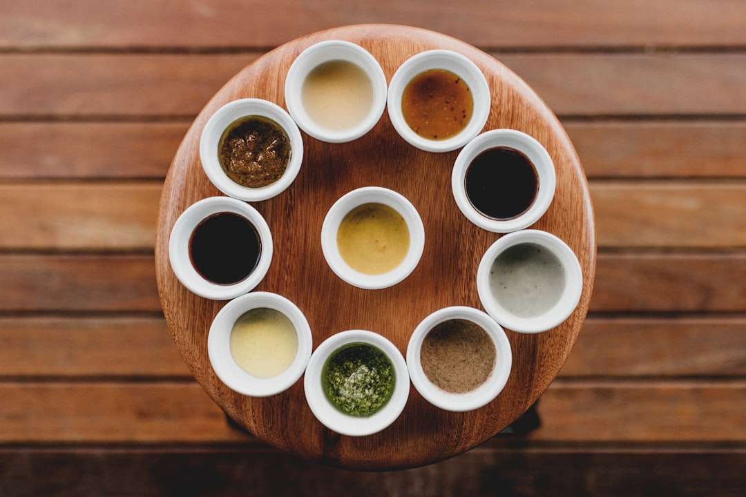 Selection of Asian sauces and spices presented in small white bowls on a round wooden tray.