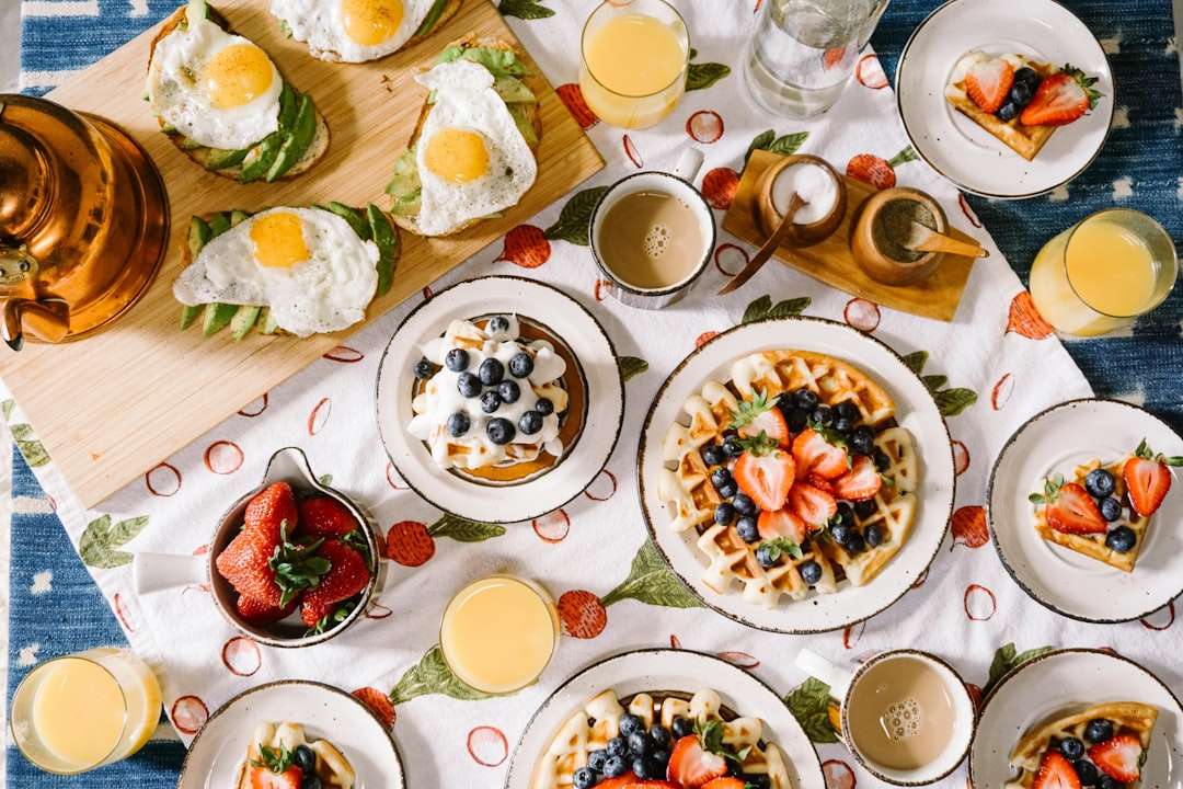 Top-down view of a breakfast table setting with strawberry waffles, fried eggs, and coffee.