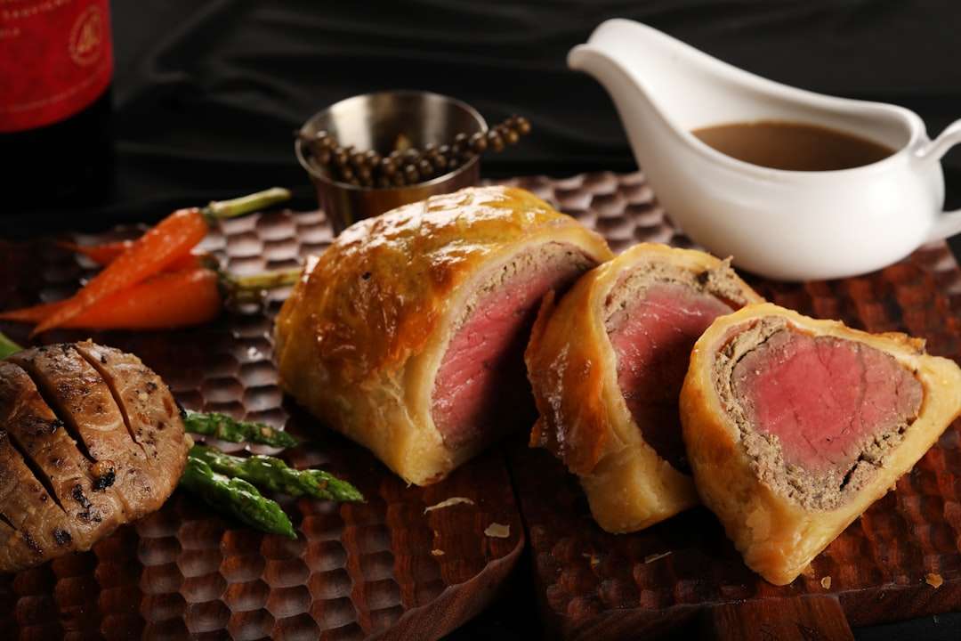 Sliced beef Wellington in a golden puff pastry crust on a serving board with gravy.