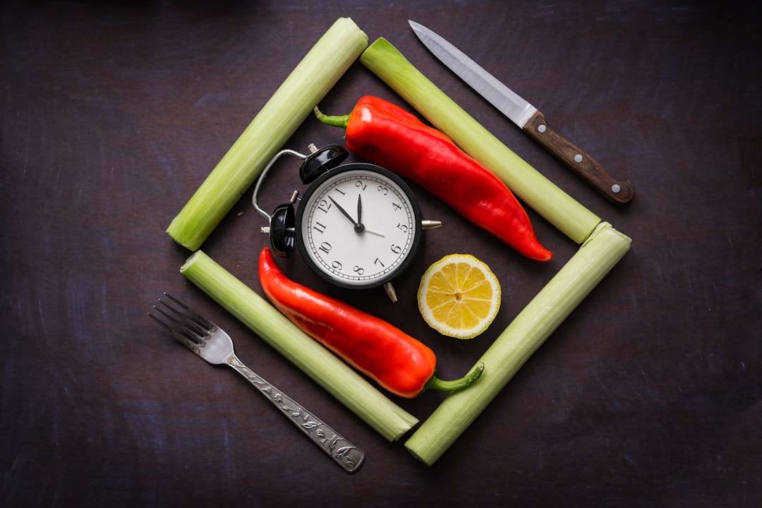 A creative food display with red chili peppers, celery sticks, a lemon slice, and a vintage alarm clock.