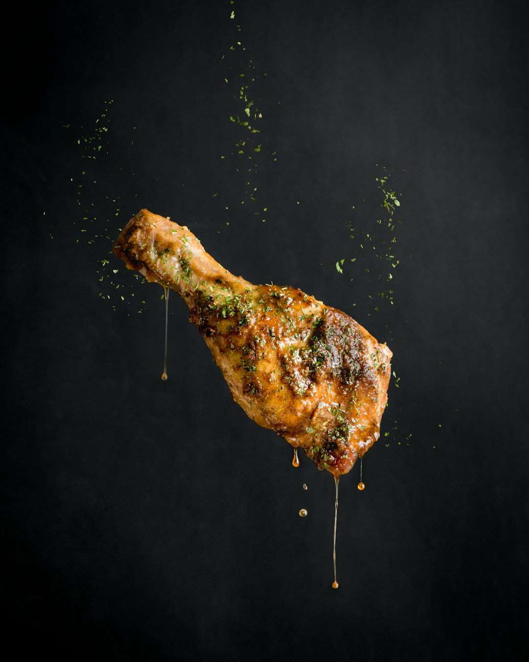 A single seasoned roasted chicken drumstick levitating against a textured black background.