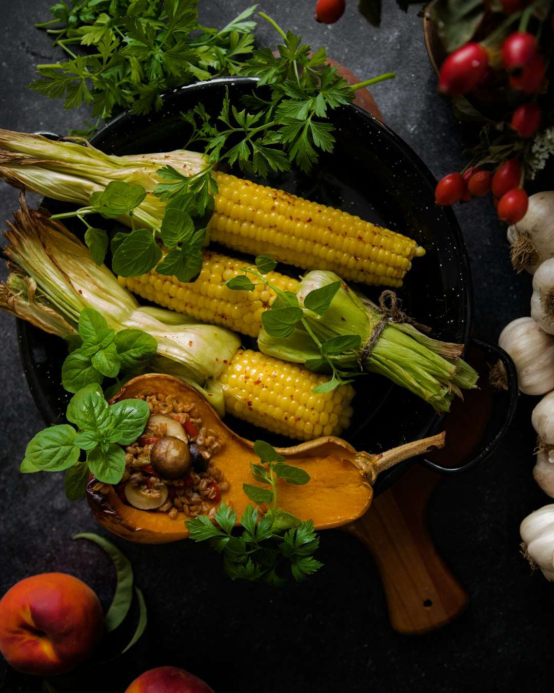 Grilled corn on the cob and roasted squash with herbs in a black baking dish.