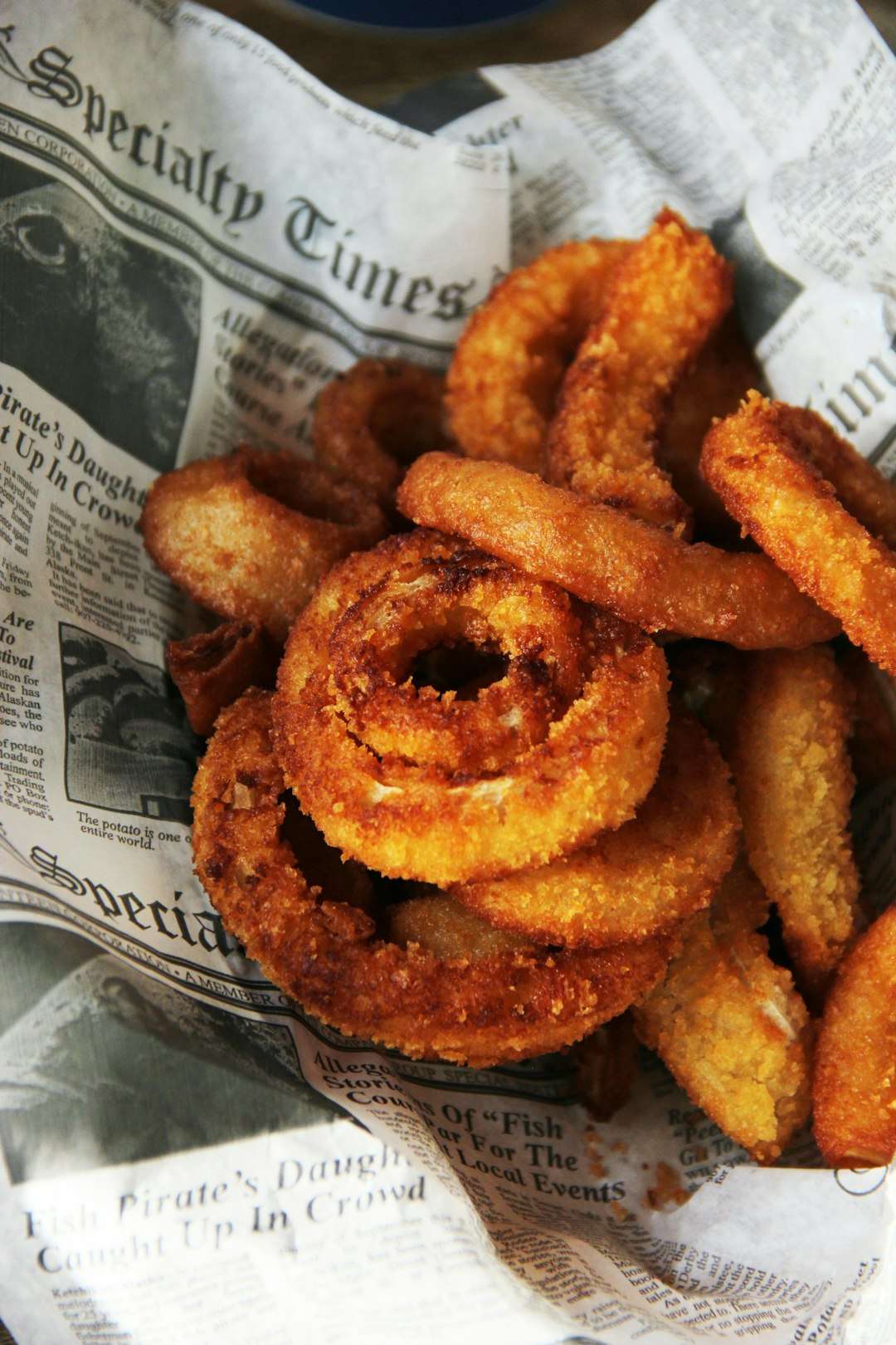 A basket of crispy, golden-brown fried onion rings served on newspaper print