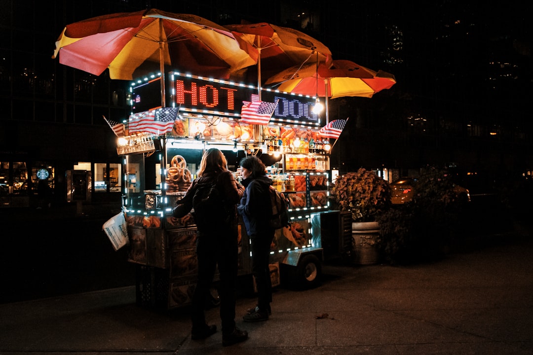 A brightly lit classic New York hot dog street food cart operating at night
