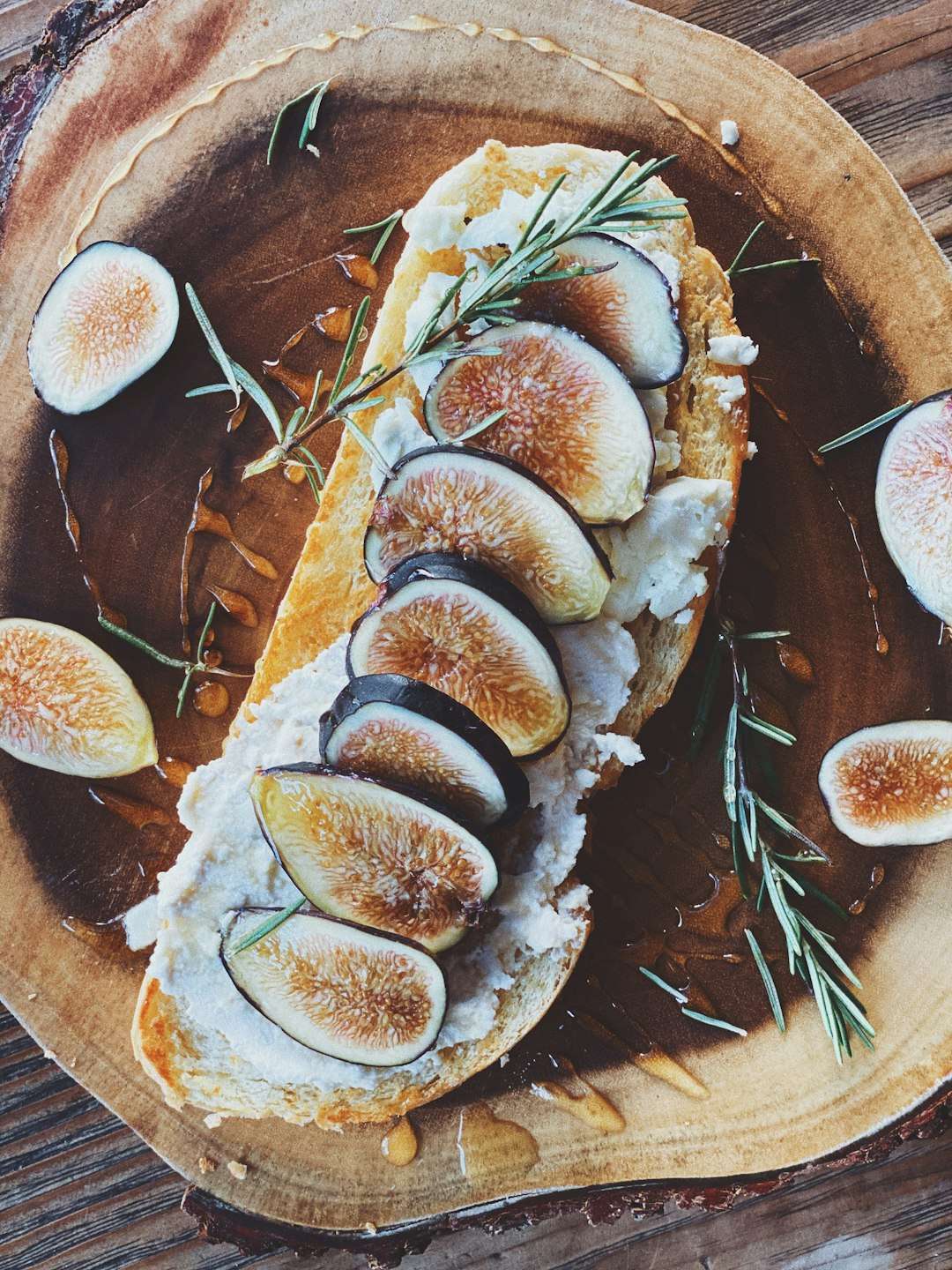 Artisanal ricotta toast topped with fresh sliced figs, rosemary sprigs, and a drizzle of honey