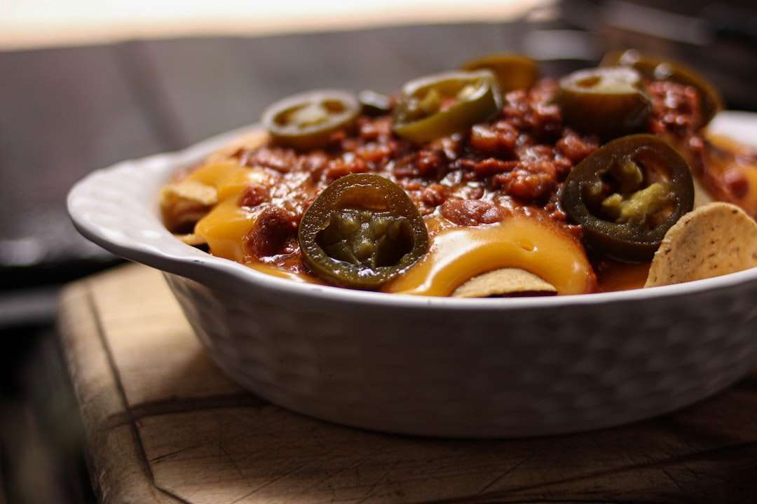 supreme-nachos-beef-guacamole Skillet of loaded supreme nachos baked with melted cheese, ground beef, sliced jalapeños, and fresh guacamole